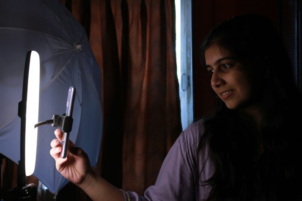 A woman holding a phone in front of a tall panel light in a dim room