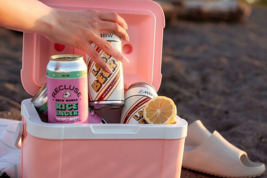 A small pink cooler filled with canned drinks on the sand at sunset
