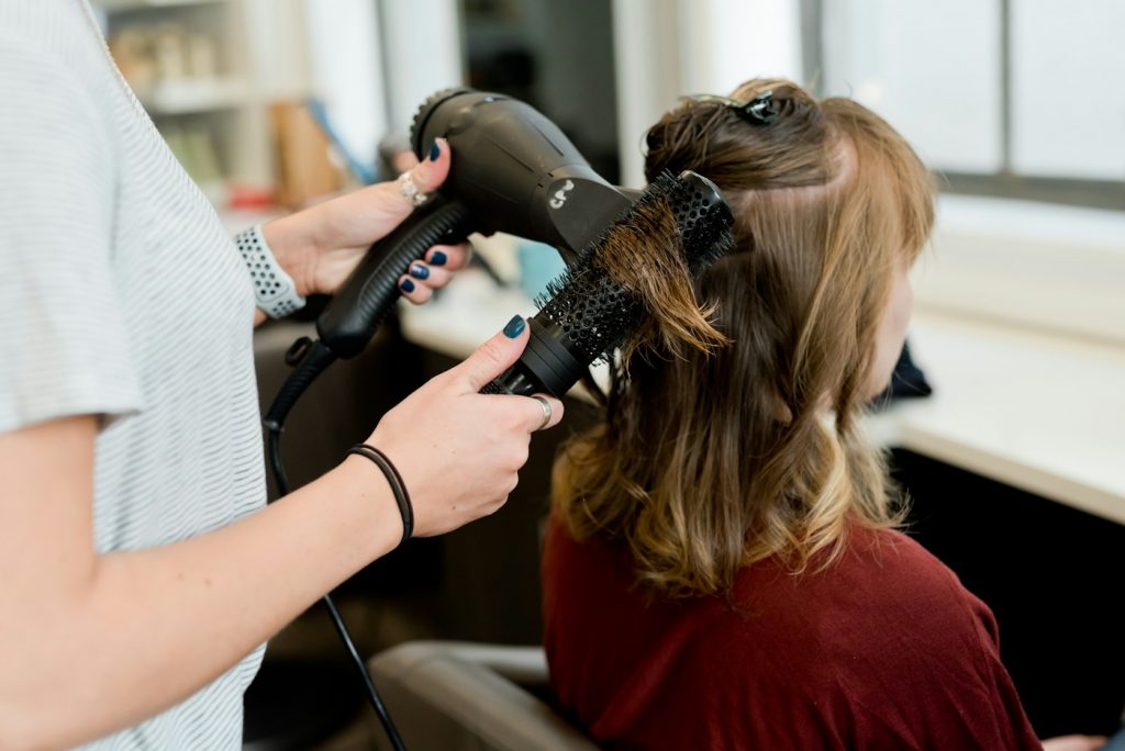Stylist blow drying a client's hair with a round brush in a salon