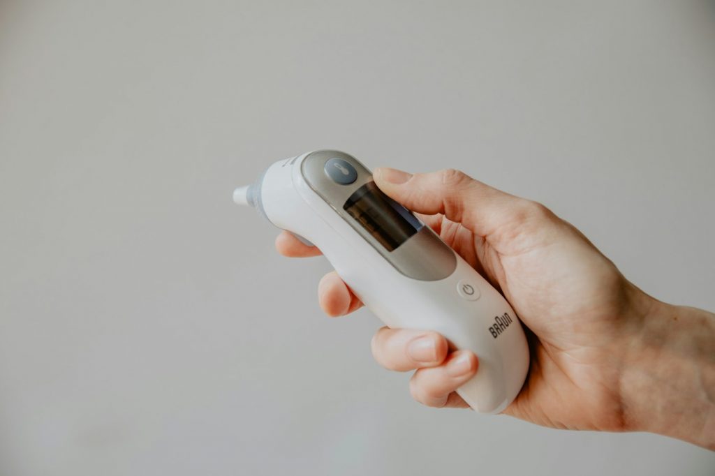 A hand holding a white ear thermometer against a plain gray background