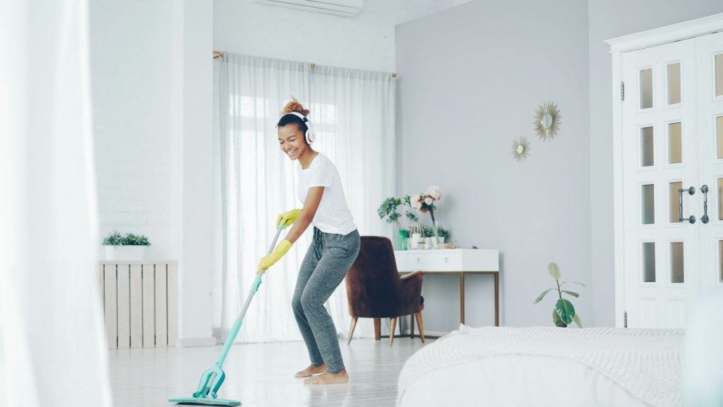 A woman in yellow gloves mopping the floor of a bright bedroom