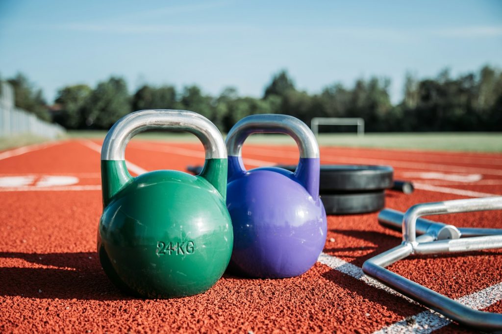 Two colored competition kettlebells on a running track with training equipment