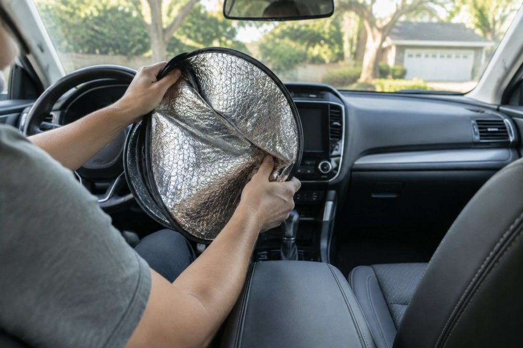 Hands folding a silver reflective windshield sun shade inside a car