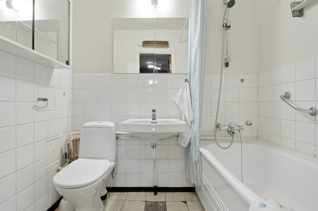 A white tiled bathroom with a toilet, sink, and bathtub with a shower curtain