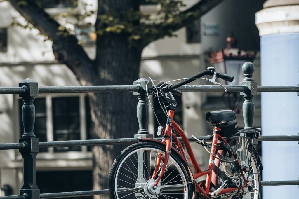 A red city bike parked against a green metal railing beside a canal on a sunny day