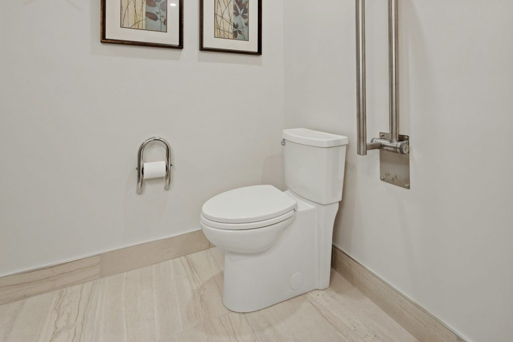 A clean white toilet in a bright bathroom with a grab bar and toilet paper holder