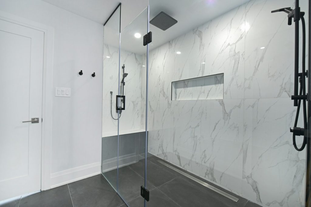 A modern walk-in shower with a glass panel, marble-look tile, and a long recessed wall niche