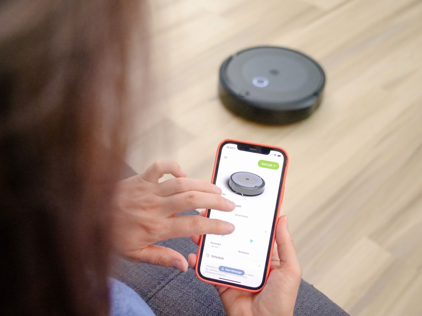 Stock photo of a person using a phone app near a robot vacuum, not a listed product
