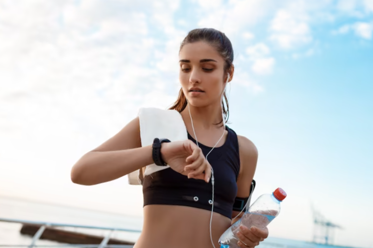 young beautiful brunette sportive girl looking at watch during sunrise over seaside.