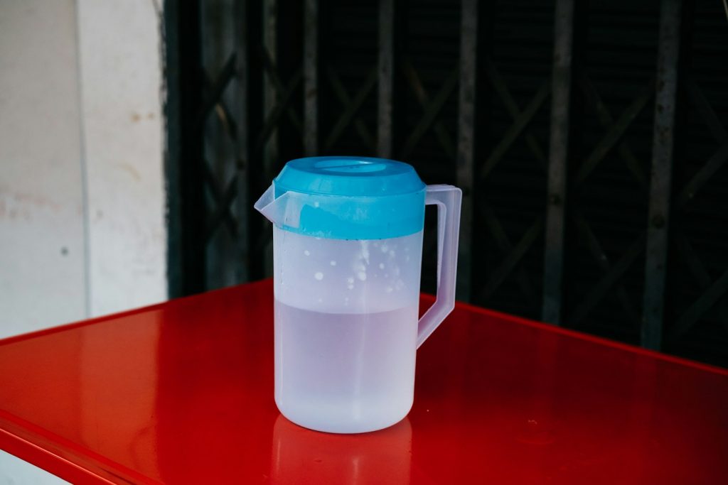 Plastic water pitcher with a blue lid on a red table