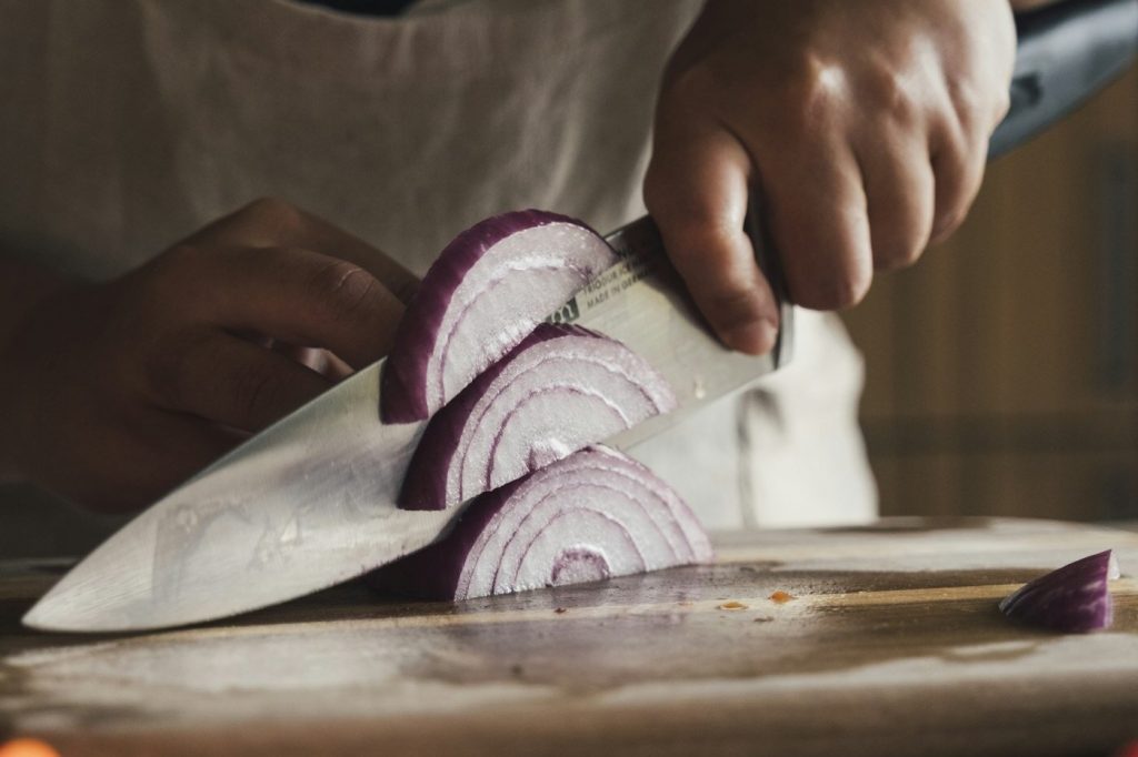 A cook slices a red onion into half rings on a wooden cutting board