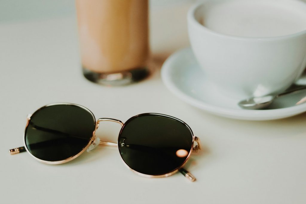 Round metal-framed sunglasses on a cafe table beside a coffee cup