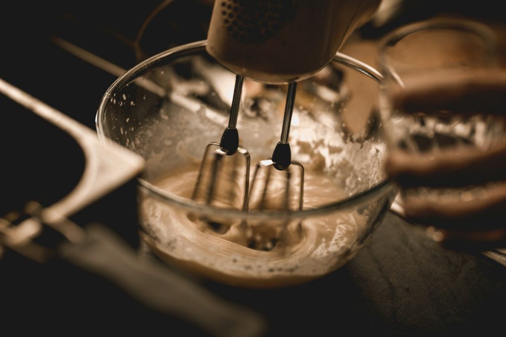 Electric hand mixer beaters whipping batter in a glass bowl