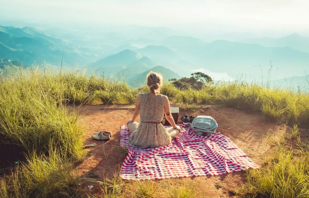 Woman sitting on a red and white checked blanket on a hilltop overlooking mountains