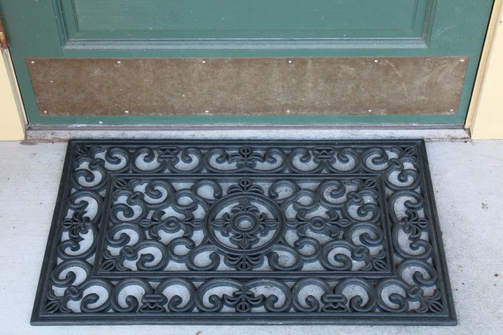 Black rubber scroll-pattern doormat in front of a green door