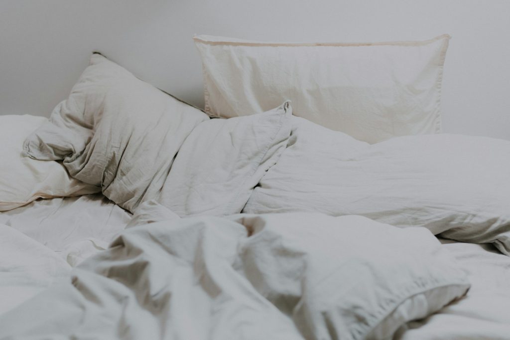 Rumpled off-white sheets and pillows on a bed