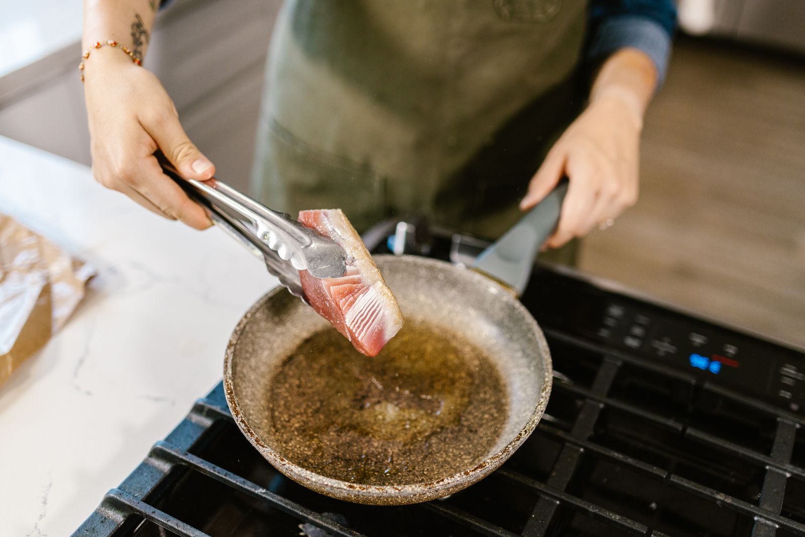 Person using metal cooking tongs to place food in a frying pan
