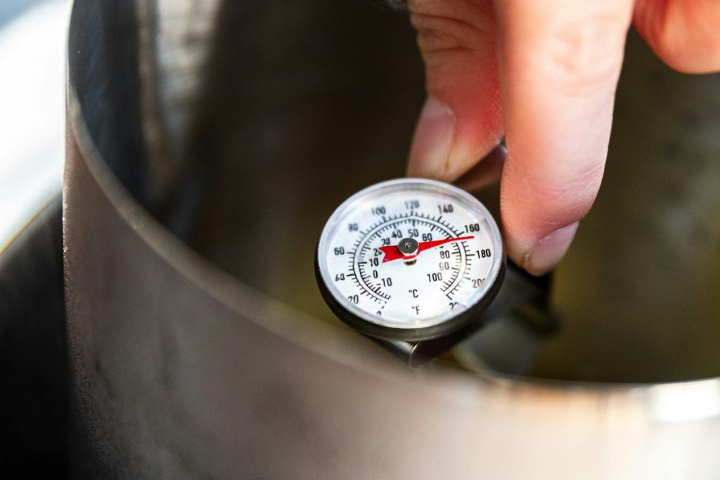 A hand holding a round analog dial thermometer inside a stainless steel cooking pot