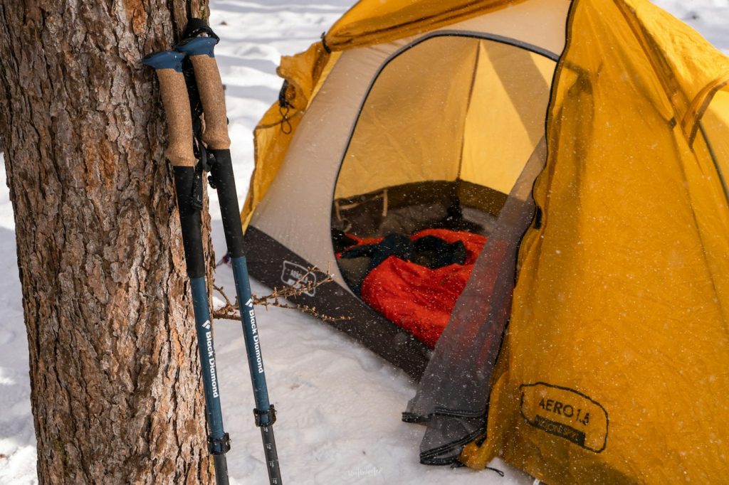 Yellow tent with a red sleeping bag inside on a snowy campsite next to a tree