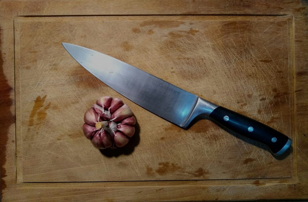 Chef knife and a head of garlic on a worn wooden cutting board