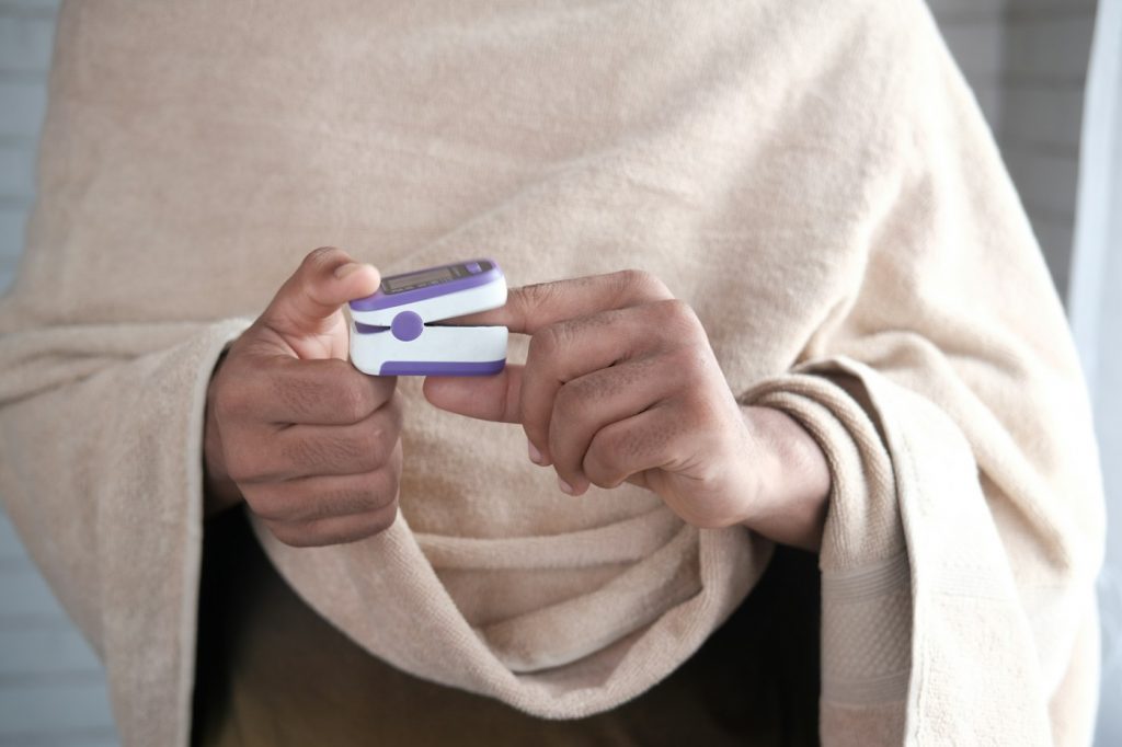 Two hands holding a small purple and white fingertip pulse oximeter