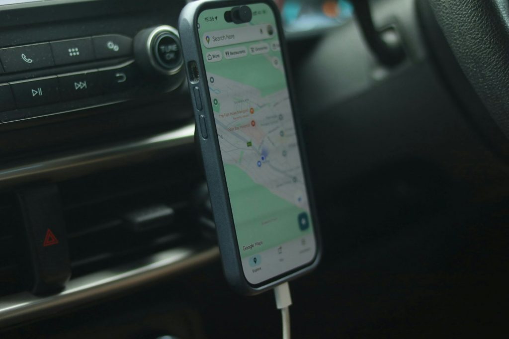 A smartphone showing a map attached to a magnetic mount beside the center console air vents of a car, with a charging cable plugged in