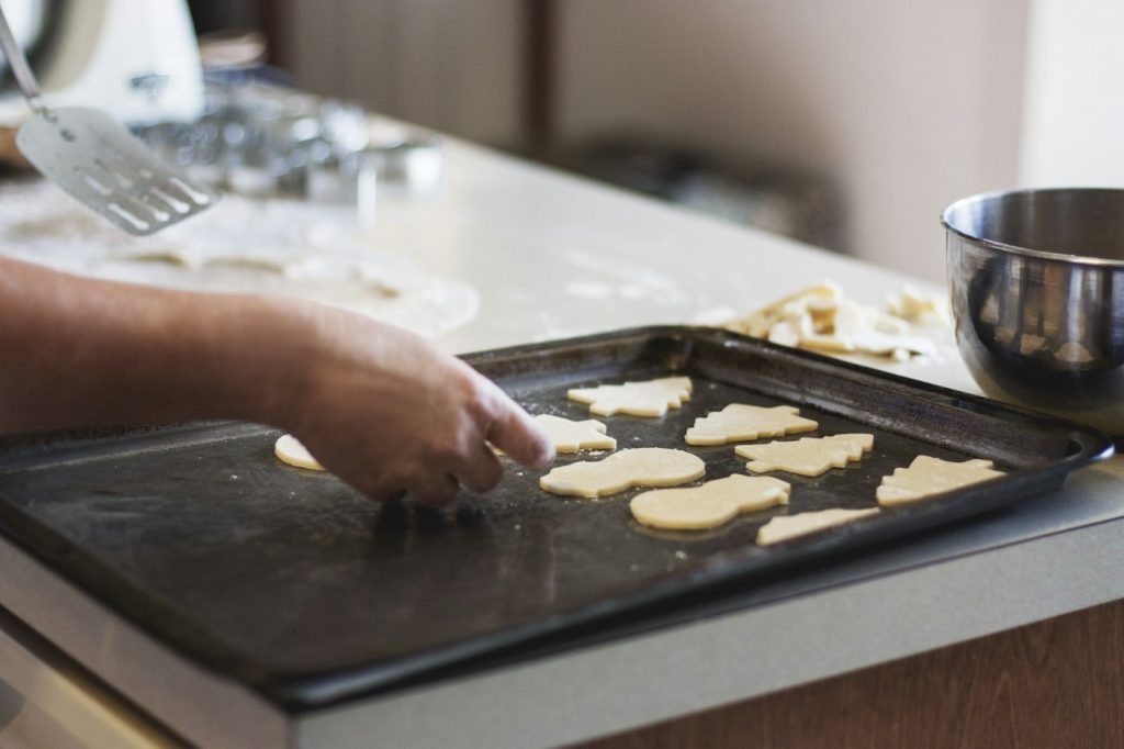 A hand placing cut-out cookie dough onto a dark baking tray on a kitchen counter