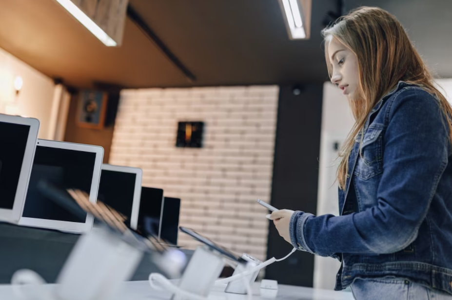 Young attractive girl in electronics store stands at desk and tests phone