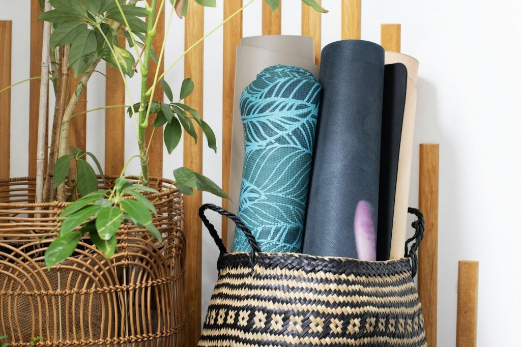 Several rolled yoga mats standing in a woven basket next to potted plants