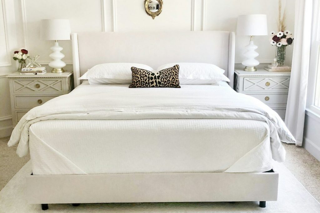 A neatly made bed with white bedding and a textured duvet in a bright bedroom