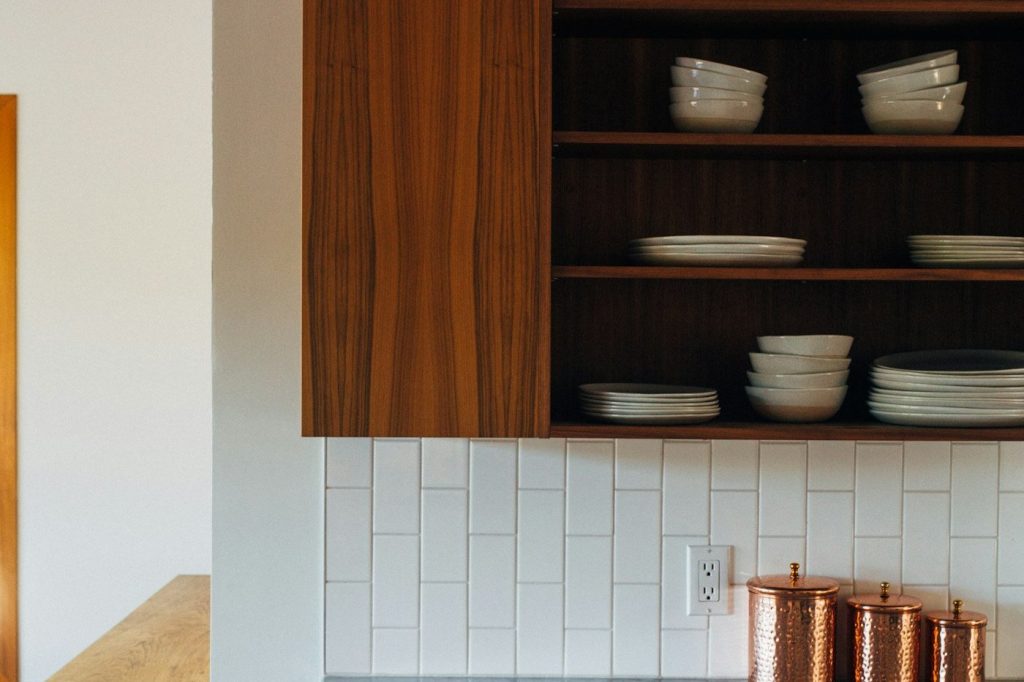 Open wooden kitchen shelves stacked with white bowls and plates above a gray stone counter