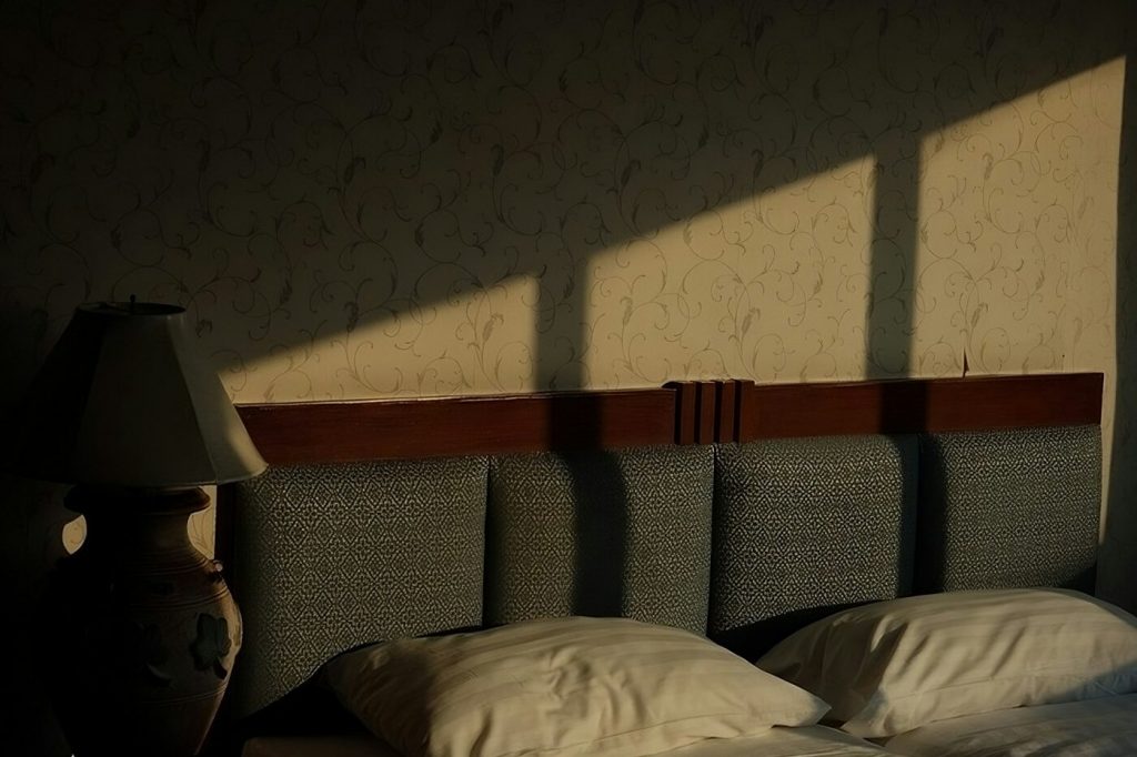 Bright bands of sunlight falling across a bed and pillows in a dark room