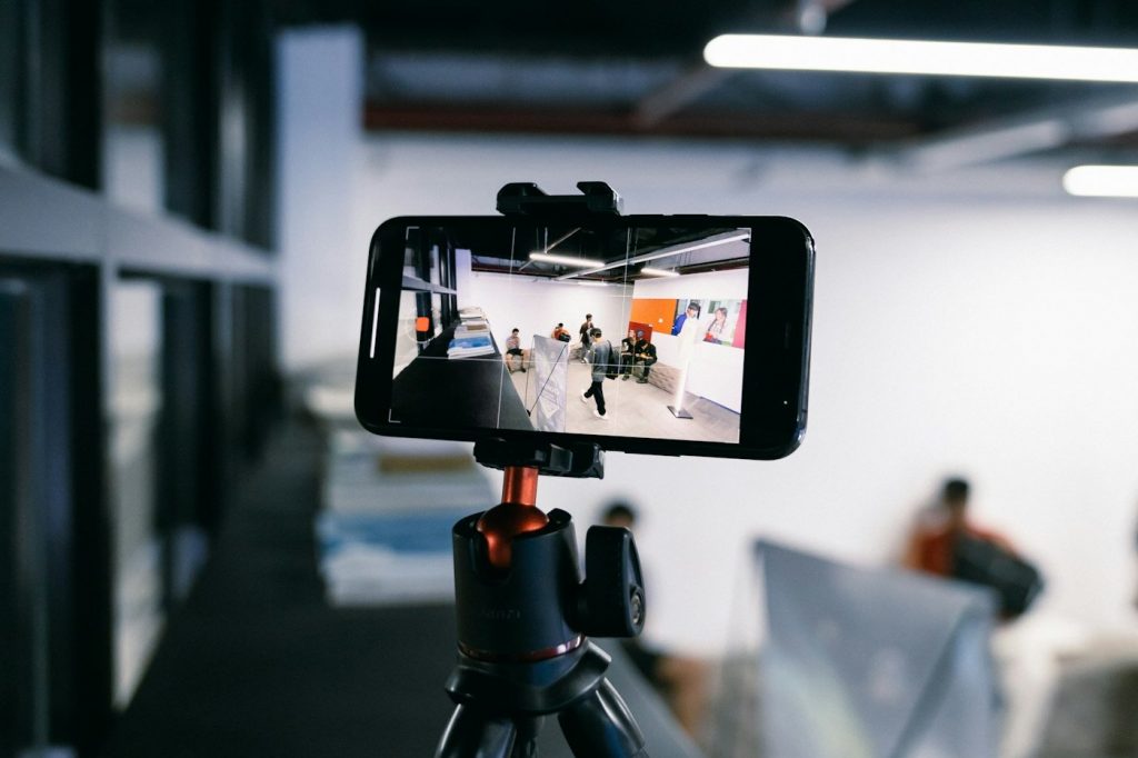 A smartphone mounted sideways on a small black tripod in an open office