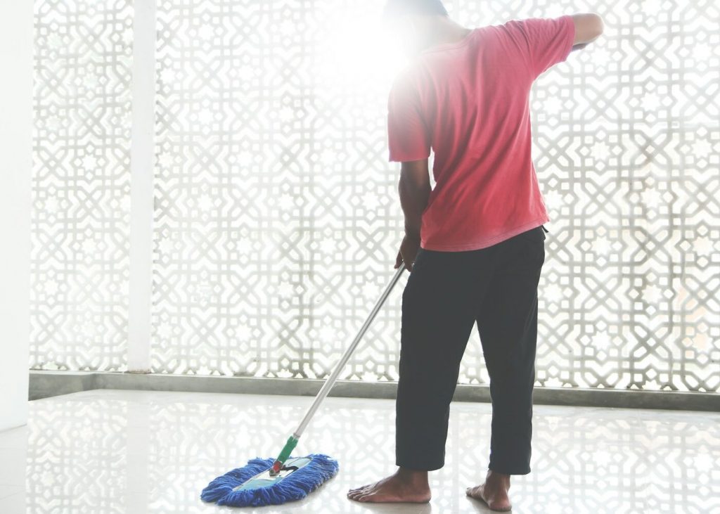 A man pushing a flat mop across a bright tile floor