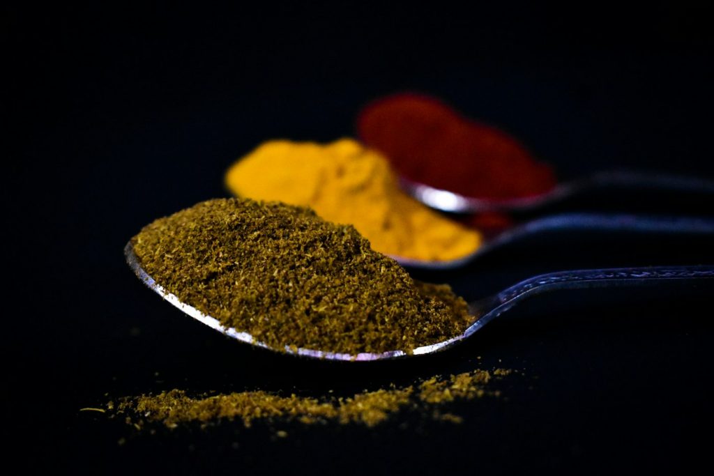 Three spoons heaped with ground spices in yellow, red, and green