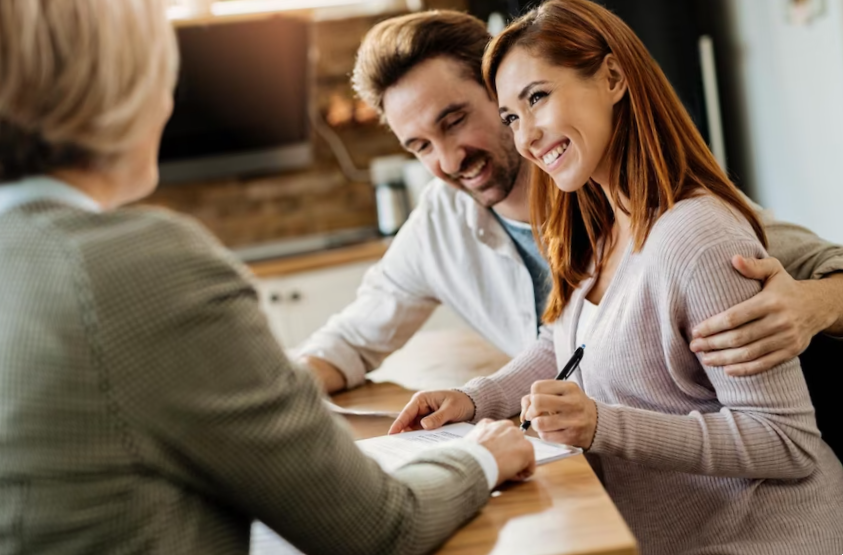 Young happy woman and her husband signing an agreement with insurance agent during a meeting