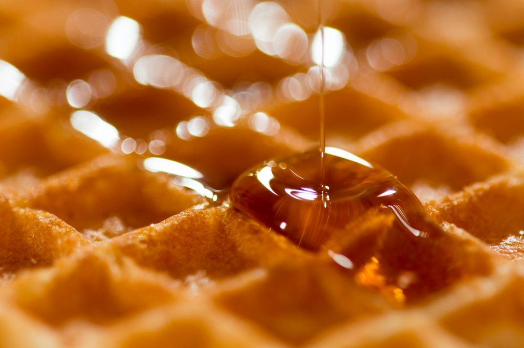 Close-up of syrup pouring onto a golden waffle