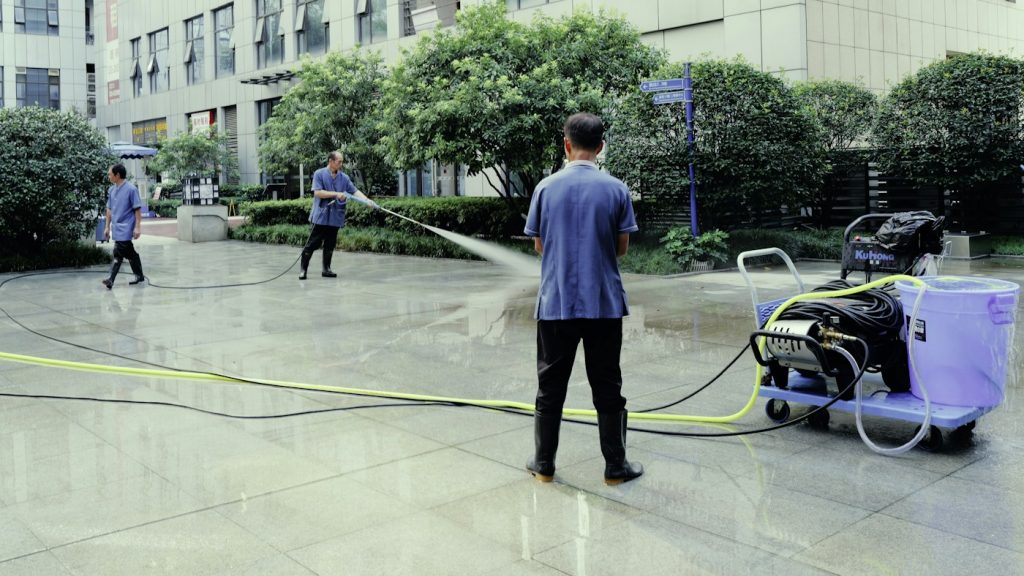 Worker using an electric pressure washer to clean a large paved plaza