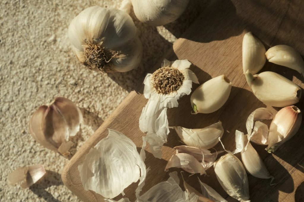 Loose garlic cloves and their papery peels on a tan surface