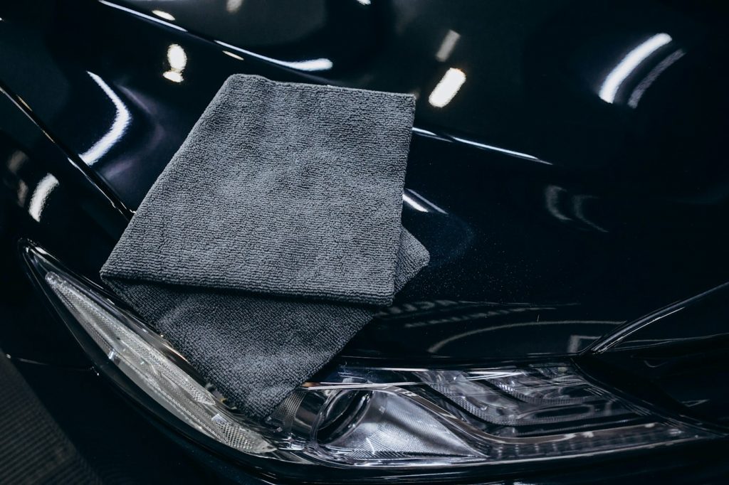 A folded gray microfiber towel resting on the hood of a shiny black car