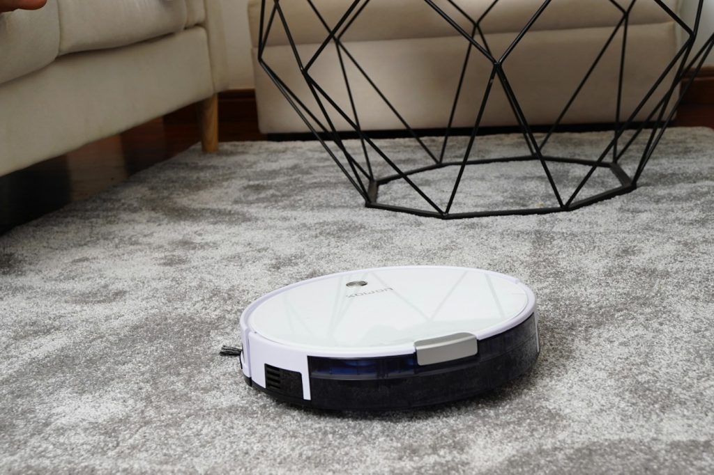 White robot vacuum cleaning a gray area rug in a living room