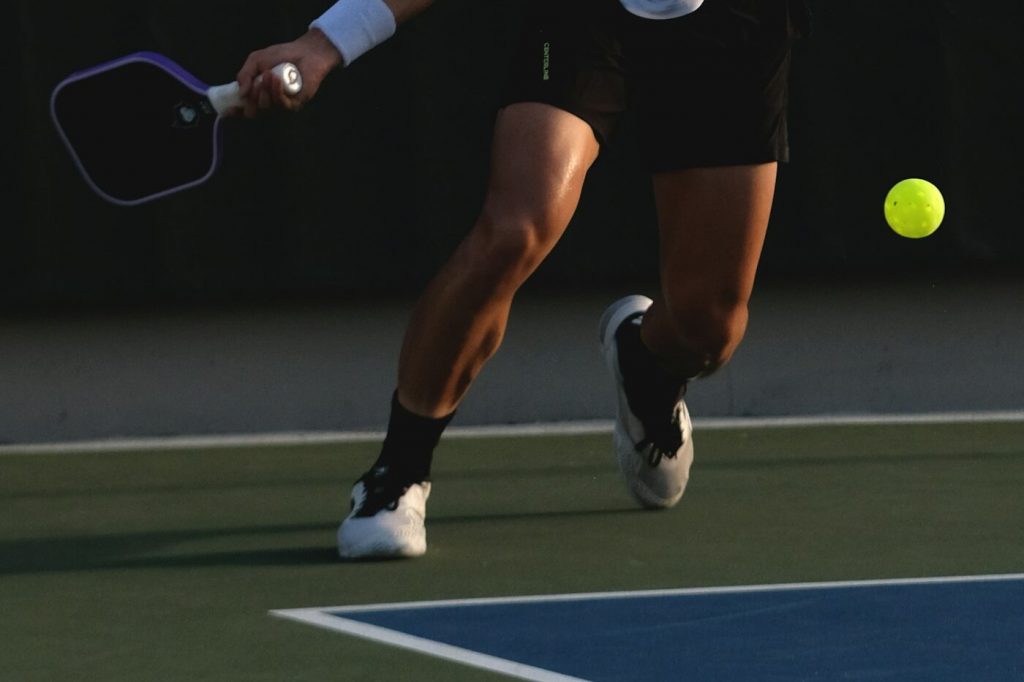 A player reaching low to hit a forehand on an outdoor pickleball court