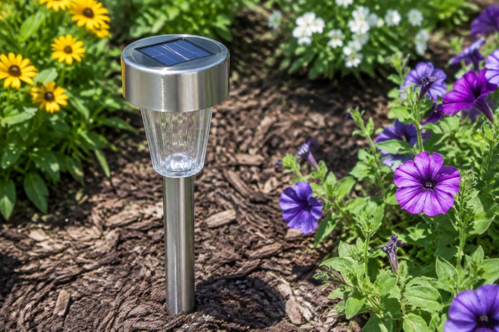 A stainless steel solar path light with its panel facing the sun in a sunny flower bed