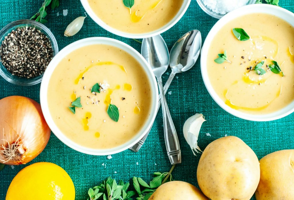 Bowls of creamy potato soup with herbs, onions, and potatoes on a green tablecloth