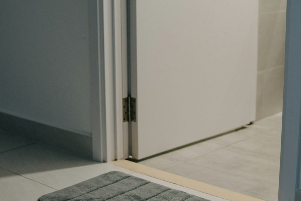 A gray ribbed bath mat on a tile floor just outside an open bathroom door