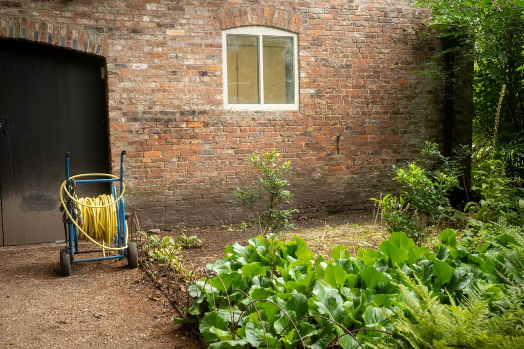 Garden hose wound on a reel cart beside a brick wall and green plants