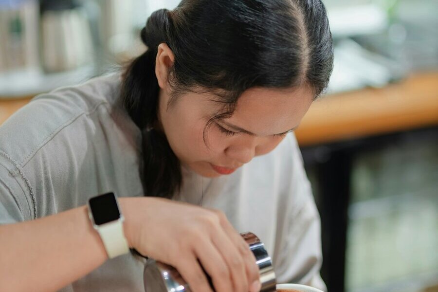 A barista pouring frothed milk into a cup of coffee