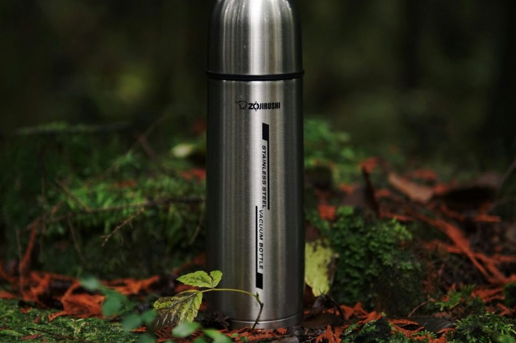 A stainless steel bottle standing among moss and leaves on a forest floor