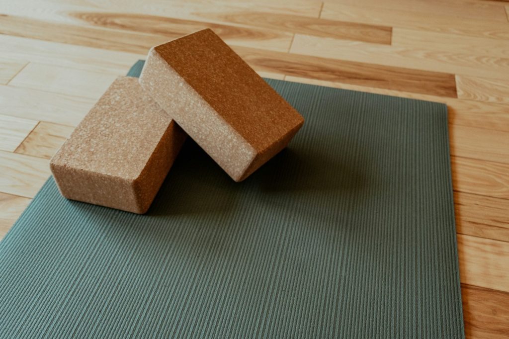 Green yoga mat on a wood floor with two cork yoga blocks