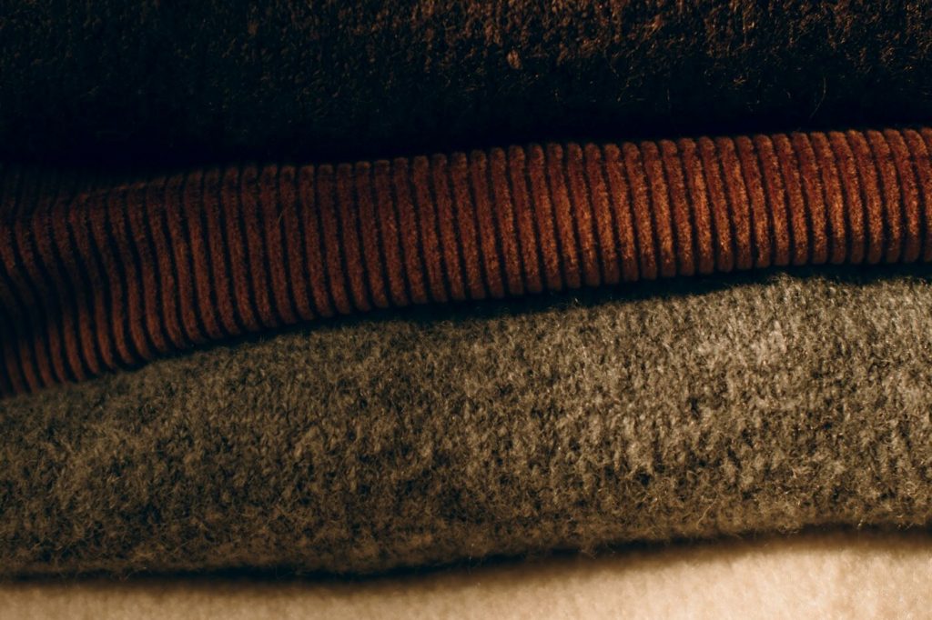 A stack of folded wool sweaters in brown, gray, and cream tones